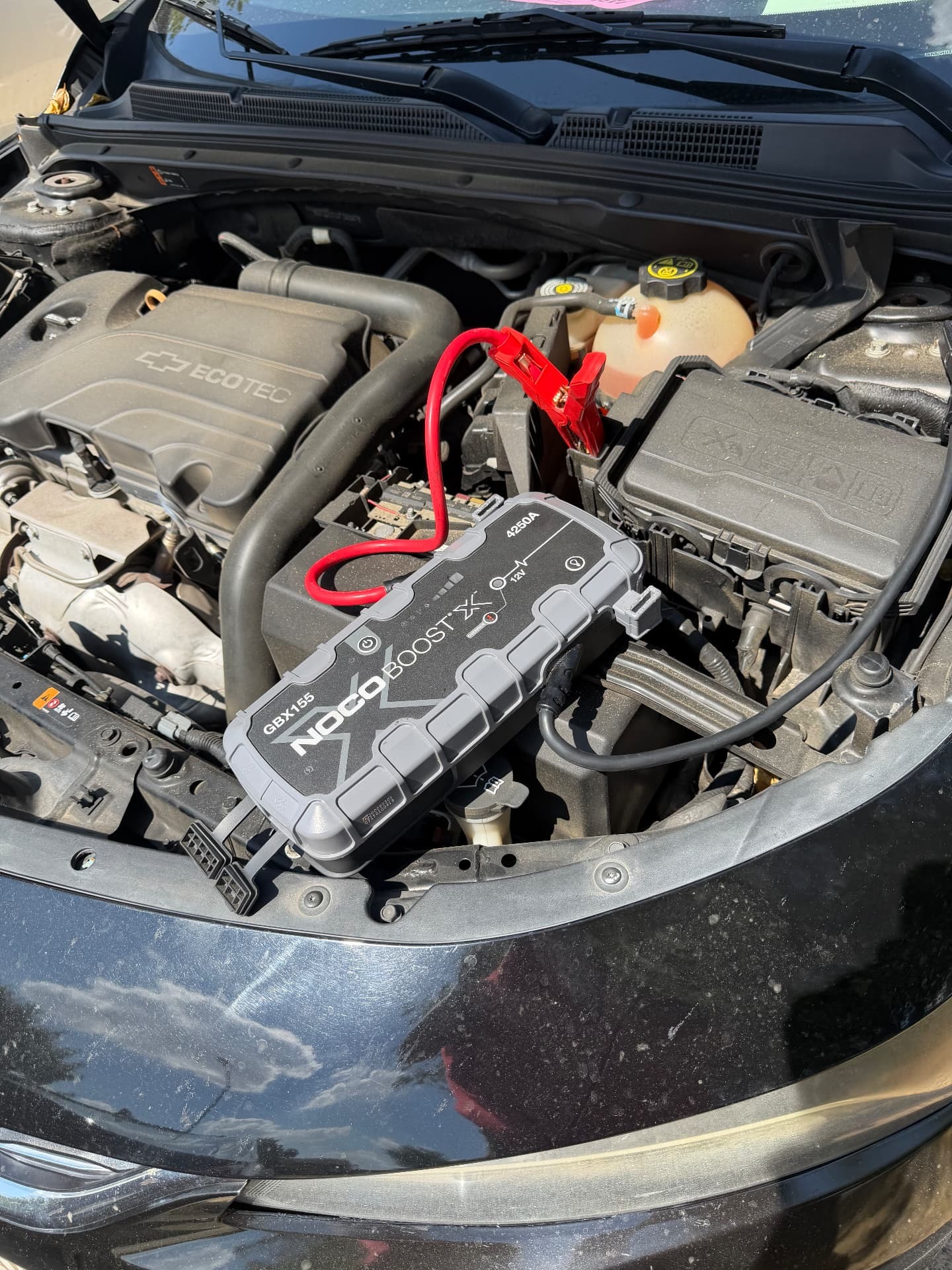 Portable NOCO jump pack connected under an open hood during a roadside jump start in Denton, Texas 76201