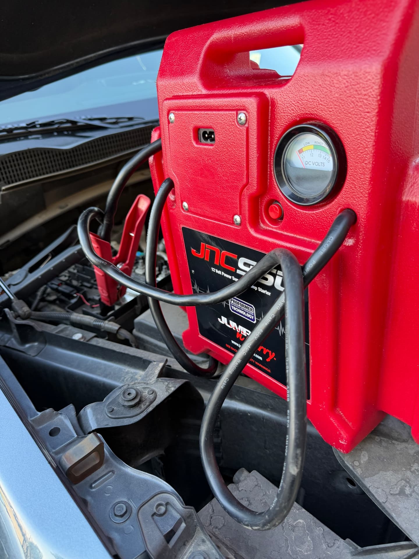 Red JNC portable jump starter connected under an open vehicle hood during a roadside jump-start call in Allen, Texas 75013