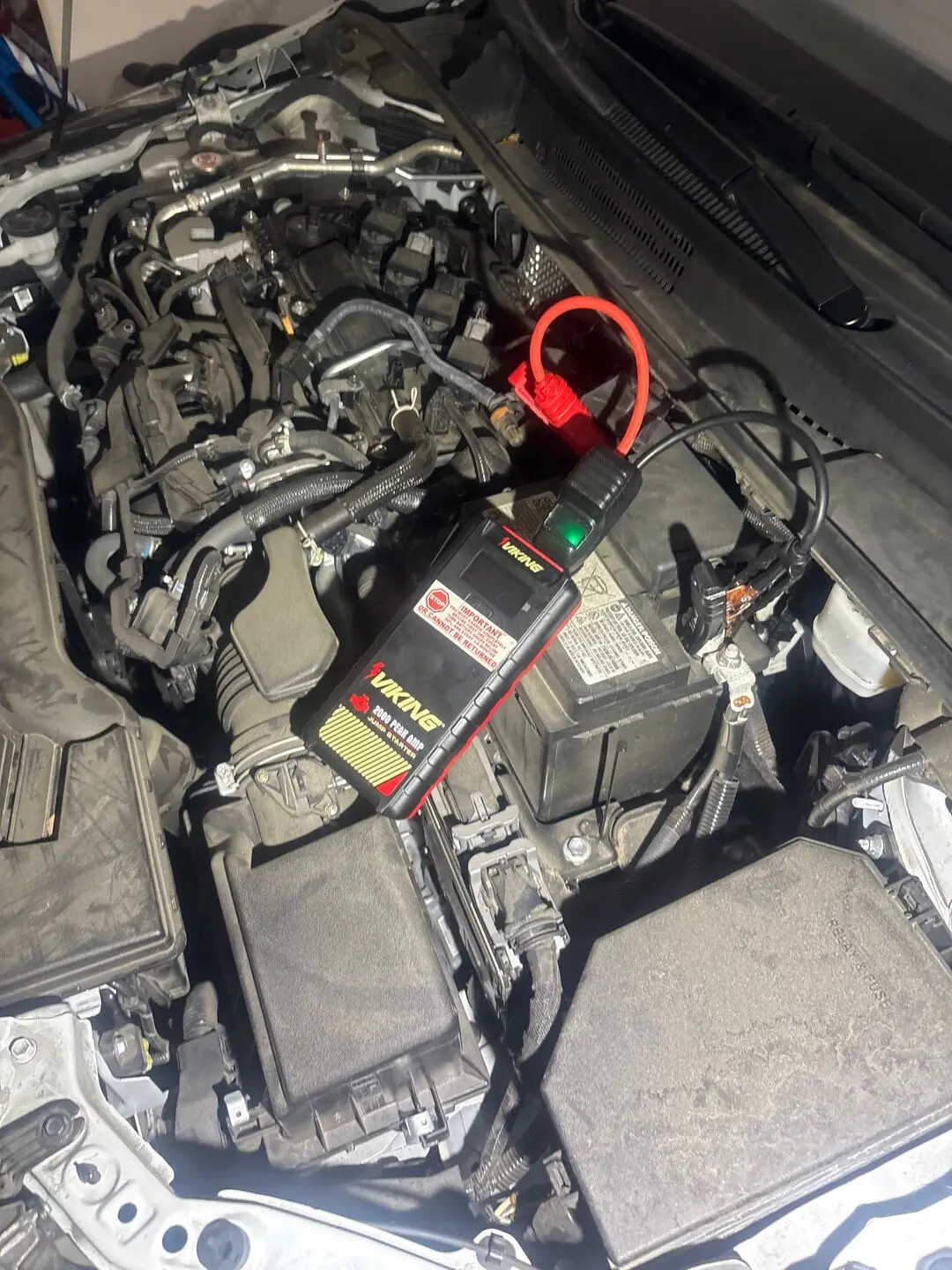Viking 2000 peak amp lithium jump pack clamped to a car battery in an open engine bay during a Denton, Texas roadside jump start