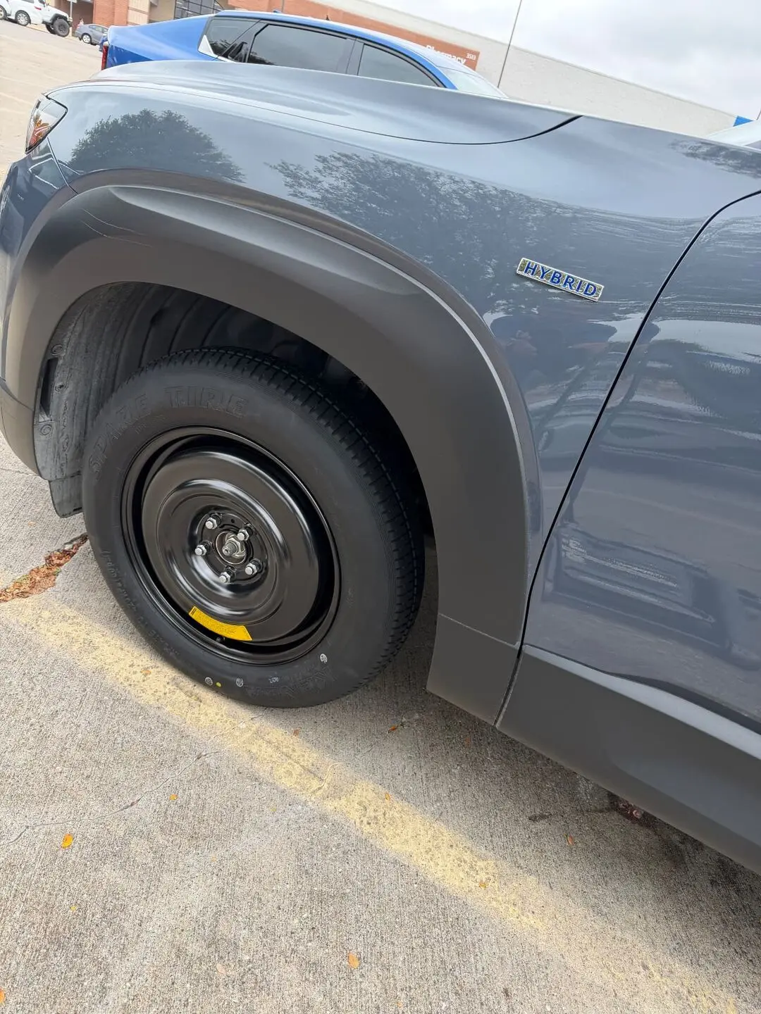 Spare tire change on a hybrid SUV in Fort Worth, TX 76102 Compact spare tire installed on the front wheel of a grey hybrid SUV after a roadside flat tire change in Fort Worth, Texas 76102