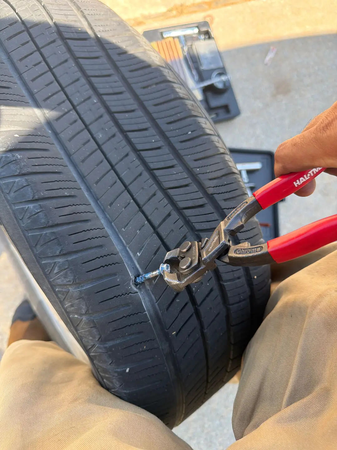 Technician using a red-handled plug tool to seat a tire repair plug in the tread of a removed tire during a Fort Worth, Texas 76109 roadside tire repair