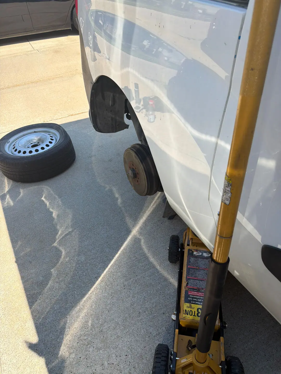 White cargo van lifted on a yellow 3-ton floor jack with the rear wheel removed and the brake drum exposed during a Fort Worth, Texas 76109 roadside tire repair