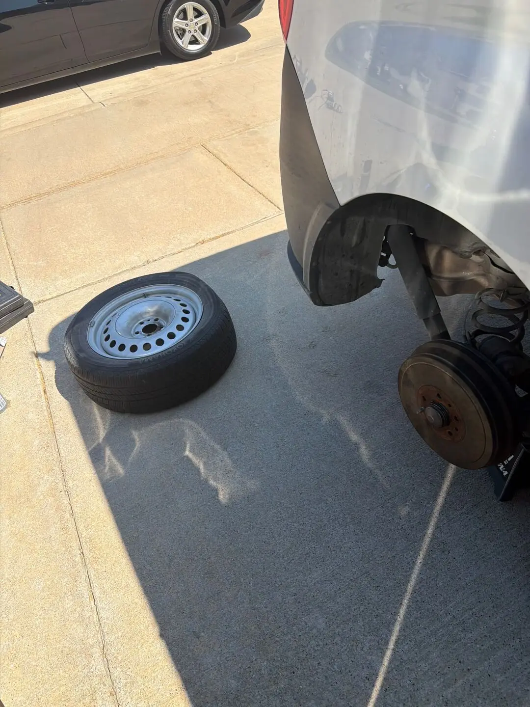 Removed steel wheel and tire lying on concrete next to a white van on jack stands with the brake drum exposed, during a Fort Worth, Texas 76109 tire repair